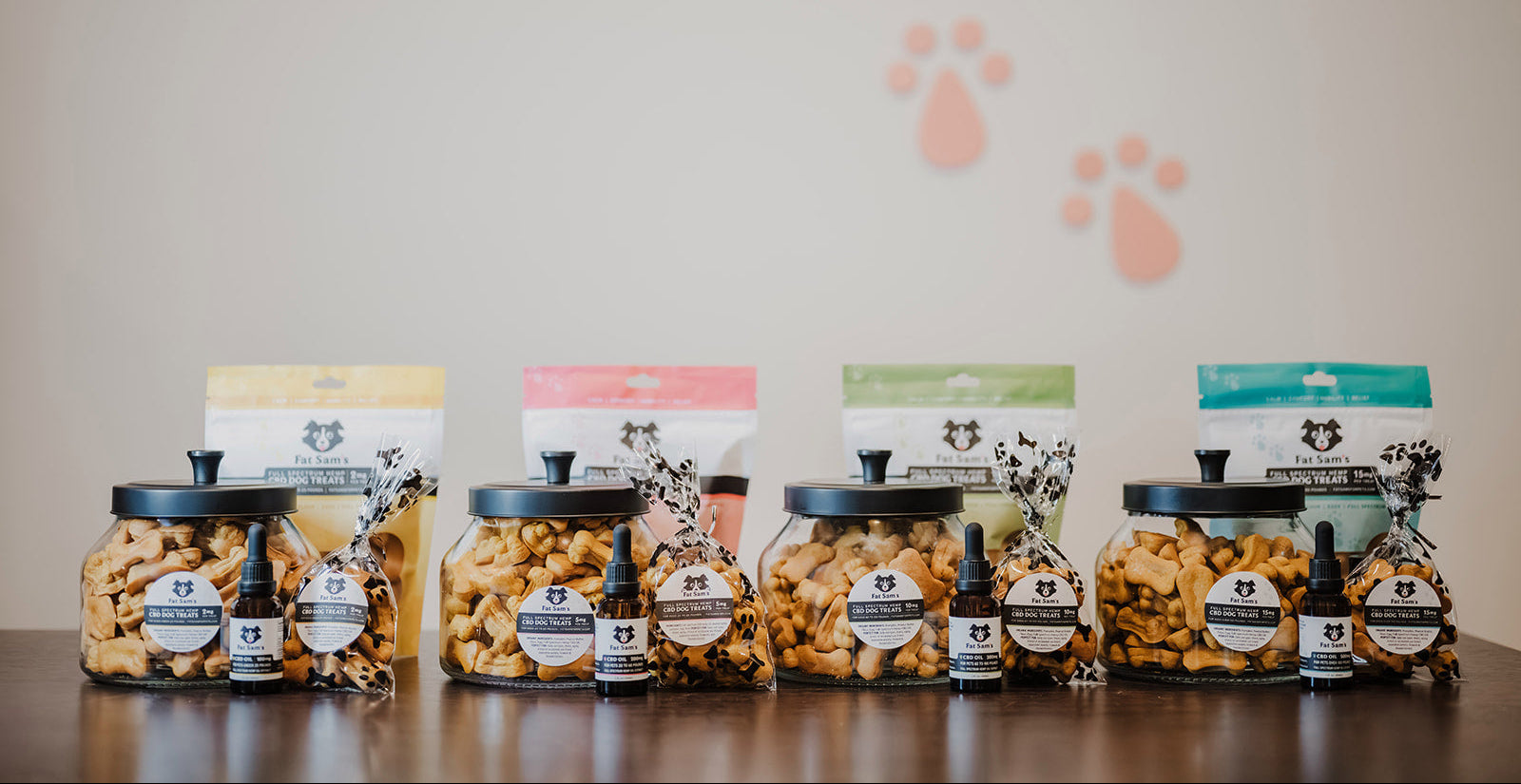 Assorted pet food products on a wooden surface with a neutral background featuring paw prints.